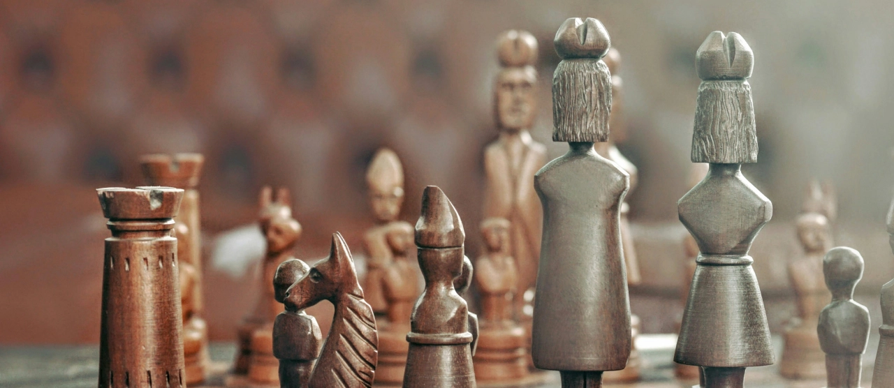 Fa sakkfigurák egymással szemben a sakktáblán, közeli nézetből. A két király egymással szemben áll.